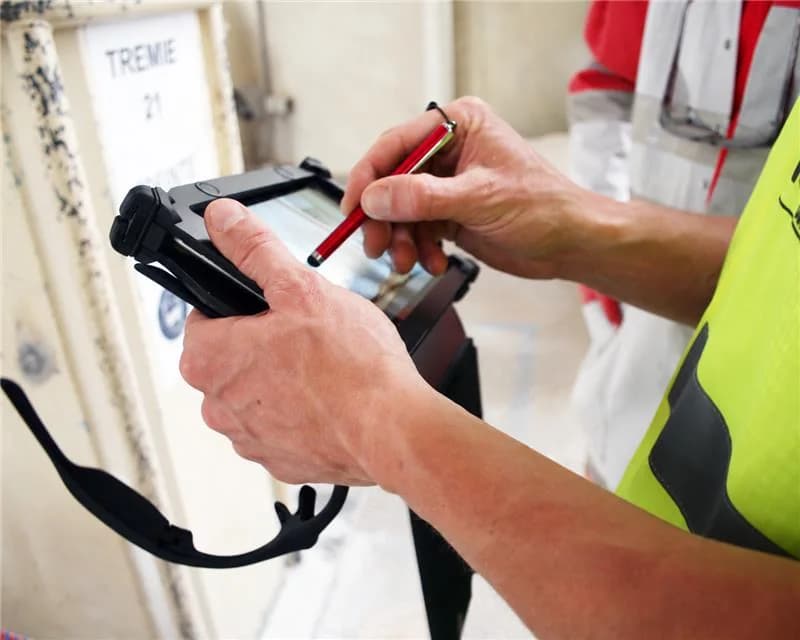A person uses a stylus to enter information on a tablet at a worksite
